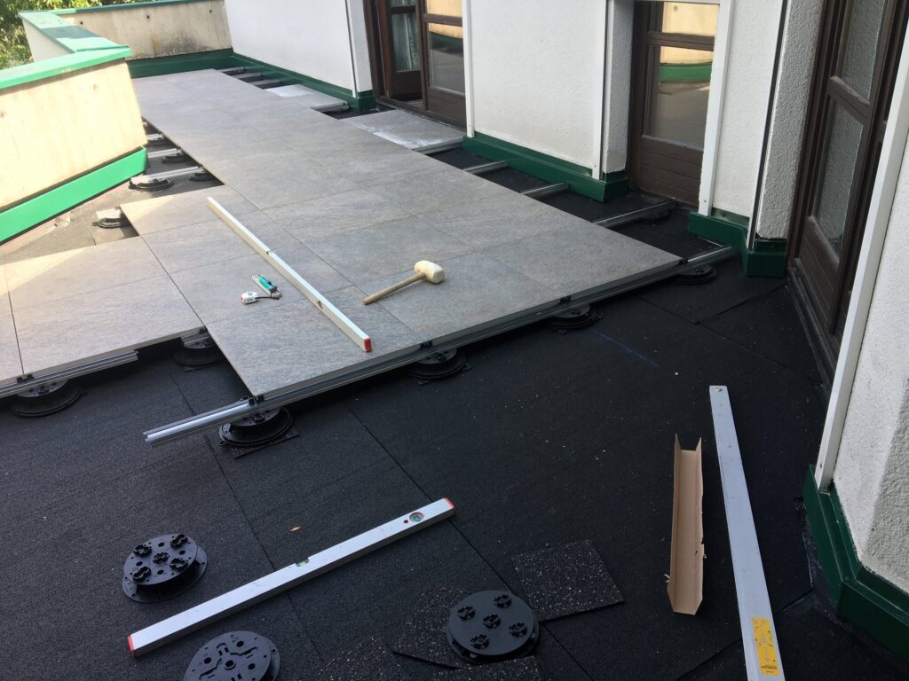 Verlegung von Terrassenplatten auf einem Schienensystem vor dem Haus